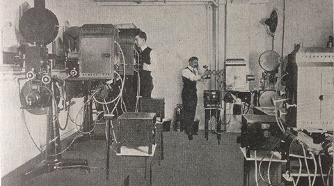A very old projection room, with two people using the machinery. (1915)