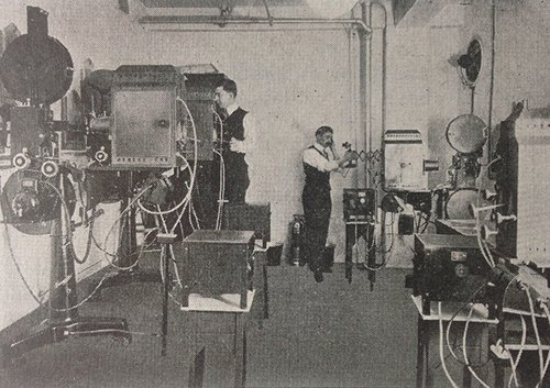A very old projection room, with two people using the machinery. (1915)