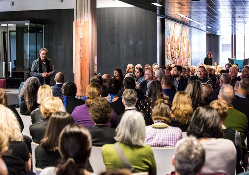 The Ngā Taonga team sitting in big group listening to a man speak.