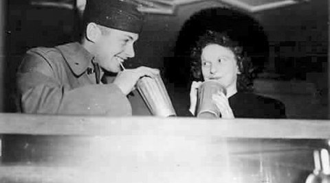 A man in uniform and a woman are drinking milkshakes.