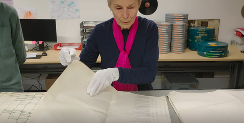 Annie Collins looking through large pieces of paper with white gloves on.