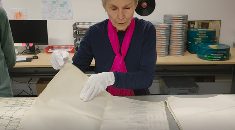 Annie Collins looking through large pieces of paper with white gloves on.