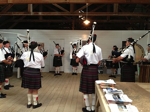 Several bagpipers are gathered inside the woolshed.
