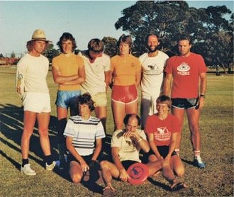 Group of guys (siting & standing) on a sports field with a frisbee.