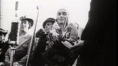 Image of Jean Batten holding flowers, after landing in Auckland.