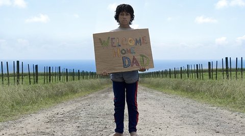 Boy in countryside holding cardboard sign.