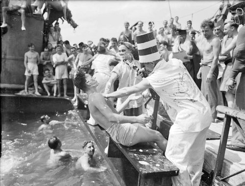 Shaved man being pushed into water with spectators aboard ship.