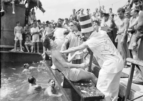 Shaved man being pushed into water with spectators aboard ship.