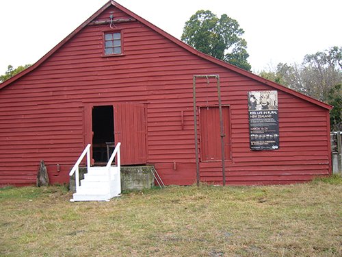A red woolshed is standing on a lawn.