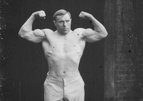 Wrestler George Hackenschmidt flexes his enormous arm muscles