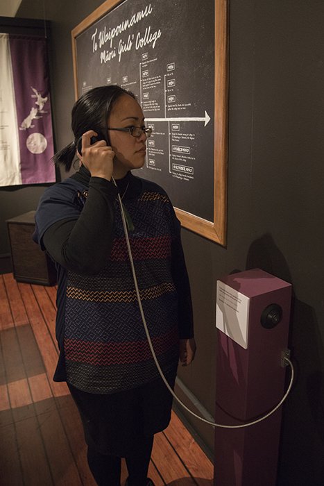A woman is standing listening to an interactive part of the exhibition through headphones