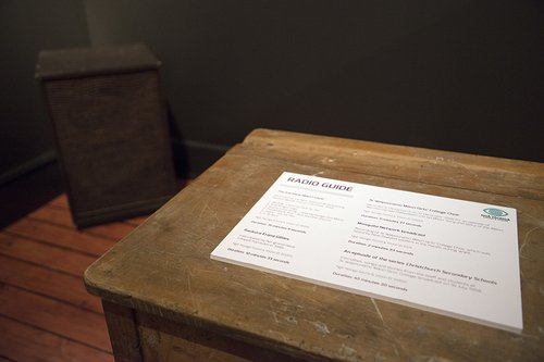 A school desk with a sign on it which reads ' Radio Guide' with a list of all the audio tracks in the exhibition.