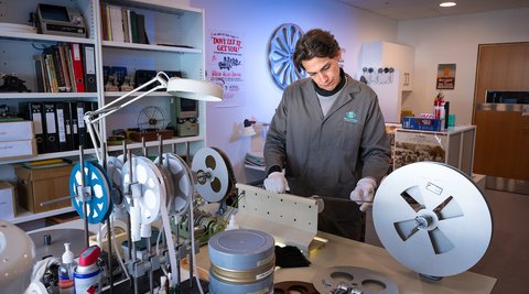 A man in a lab coat winding film in a preservation suite