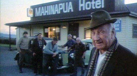 A screenshot of an old Mainland cheese TV ad. An older man stands in front of the Mahinapua Hotel with a group of other men behind him, leaning on a car.