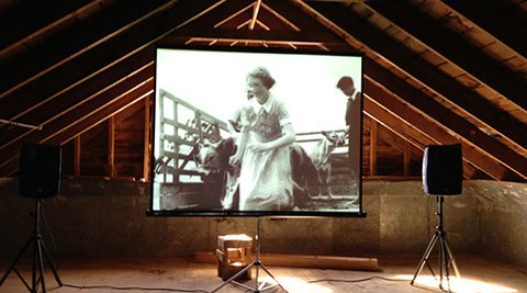 A movie screen inside a woolshed is playing a film.