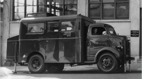 An old New Zealand Broadcasting van is parked. A man can be seen peering out of one of the windows.