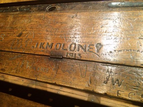 The name J.K.M Moloney 1915 is carved into a wooden desk