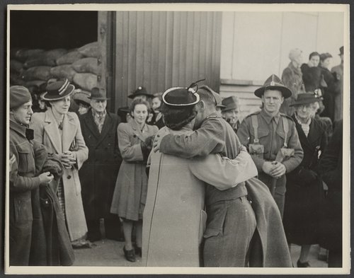 A crowd of people are watching a man in a soldier's uniform and a woman embracing.