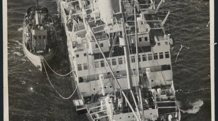 A large ship has hit a reef. A smaller boat is nearby.
