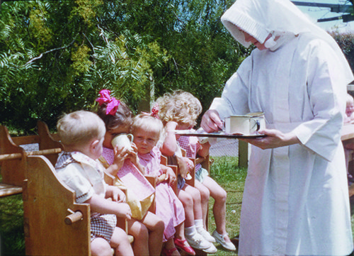 A convent nurse providing drinks for children.