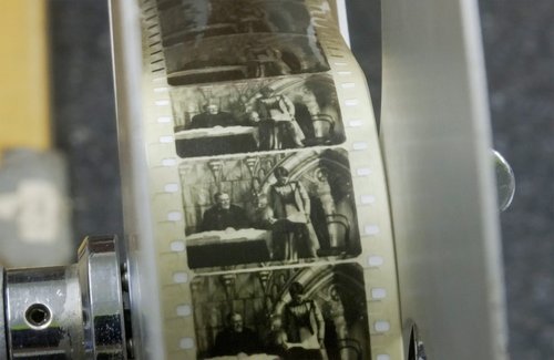 A close up on a reel of film depicting a woman standing and a man sitting at a desk.