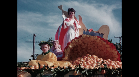A beauty queen and two children on an orange-themed parade float