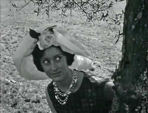 A woman in a big organza hat is peering around a tree