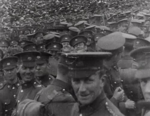 A soldier stands in front of a crowd of other soldiers looking into the camera.