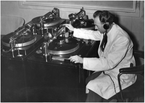 A man in a white coat operates complicated looking audio equipment
