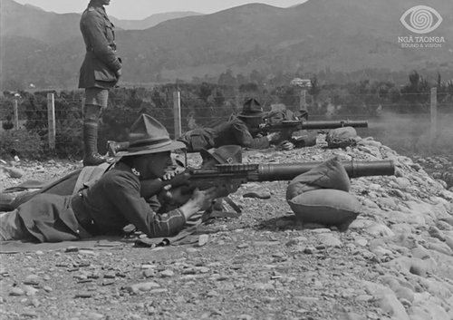 Two soldiers are lying on the ground preparing to shoot with rifles. Another soldier is standing nearby.