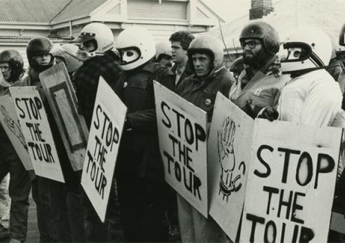 Men protesting the 1981 South African rugby tour - they are wearing motorcycle helmets, holding signs that say 'Stop the Tour'.