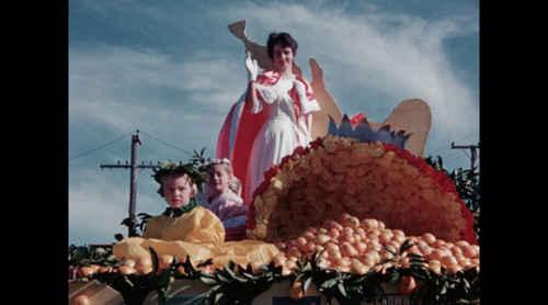Still from a film by Tauranga amateur filmmaker Norman Blackie - Woman and two children on a float filled with oranges.Float filled with oranges