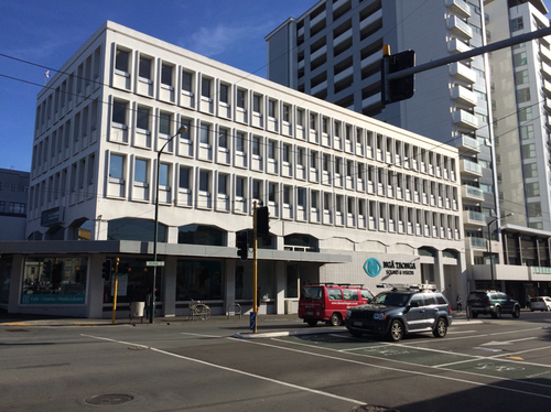 Te Anakura - the old Ngā Taonga building on Taranaki Street in Wellington. A large white building is in front of a busy street with two cars in motion.