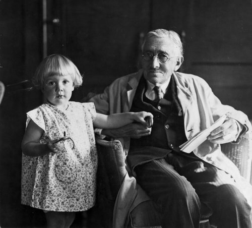 An older man, Truby King, sits in a chair, with a small child, Madelaine beside him.