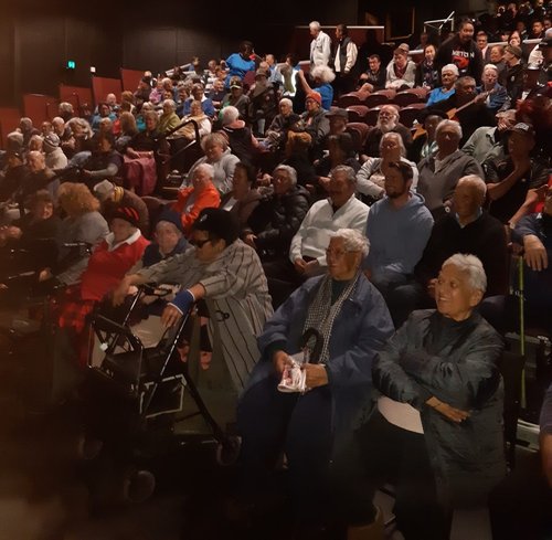 A small crowd of kaumatua are gathered in a cinema for a film screening.