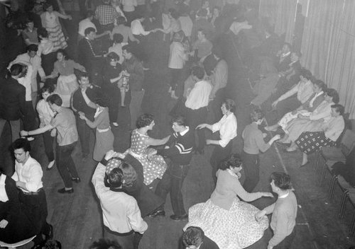 A large group of people are rock and roll dancing in a dance hall.