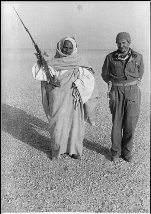 Two men posing in the desert with a long gun