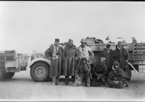 A group of men in heavy coats pose beside a truck in the desert