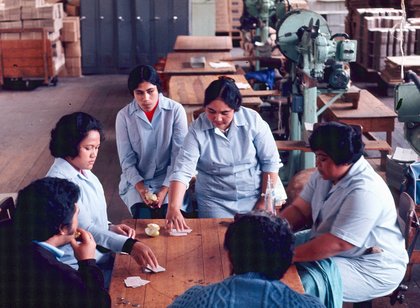 A group of Pacific Island women sit around a table at work during a break.